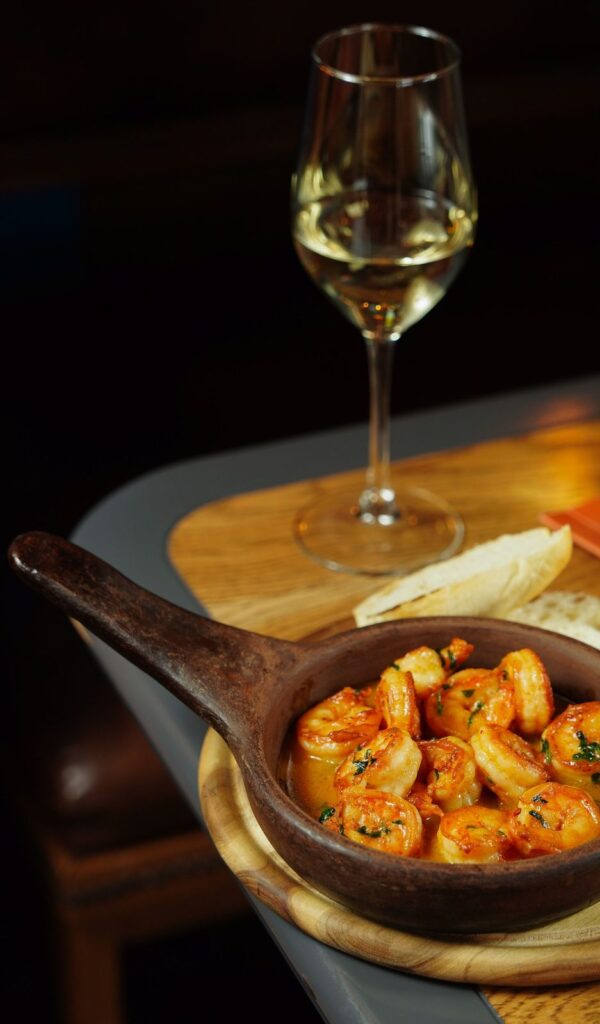Gambas al ajillo en una cazuela de barro junto a una copa de vino blanco