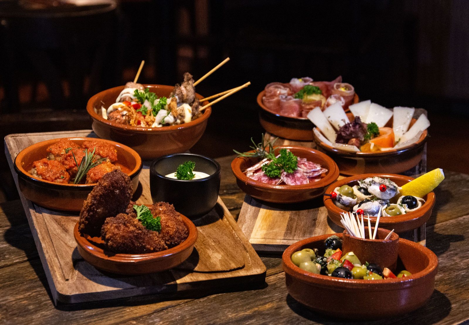 Tapas variadas servidas en cazuelas de barro sobre tablas de madera
